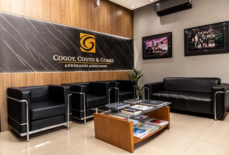 Recepção do escritório CCG com poltronas de couro preto, mesa de centro com revistas e logotipo retroiluminado na parede.