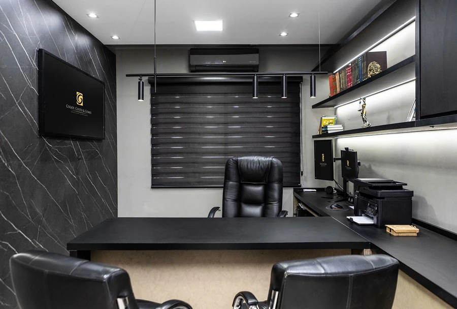 Escritório de Alex Sandro do Couto com decoração minimalista, mesa escura, cadeiras executivas e estante com iluminação embutida e livros jurídicos.
